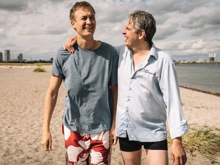 Zwei Männer gehen lachend am Strand entlang.